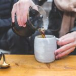A glass french press and a filled mug of french press coffee on a wooden table