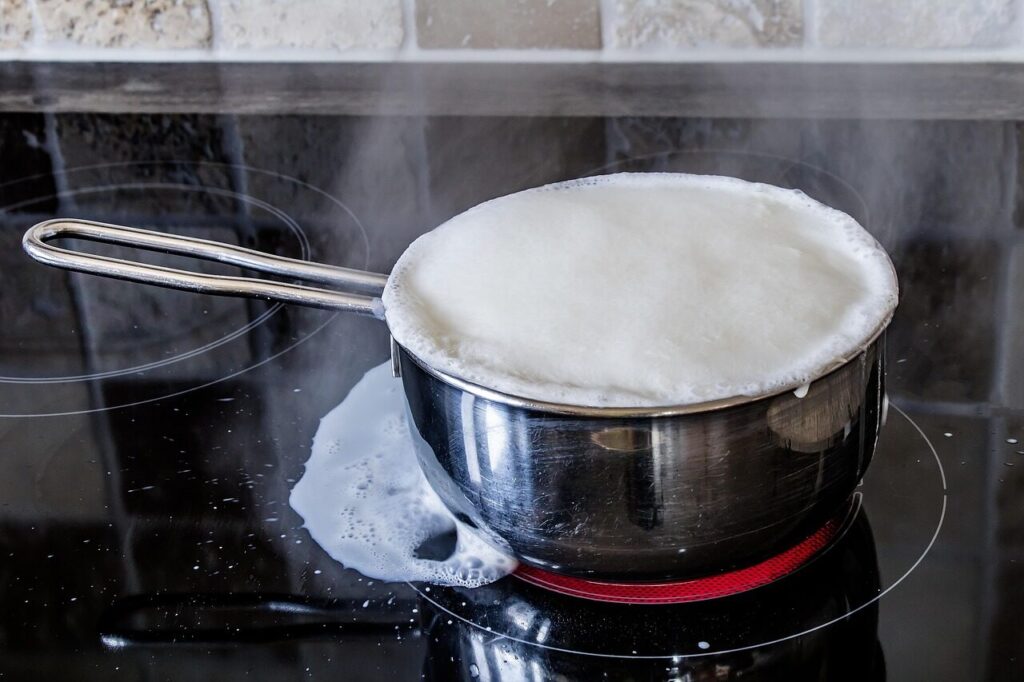 A metal whisk beating warm milk into foam in a small saucepan