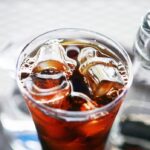 A tall glass of iced coffee with large ice cubes on a wooden table