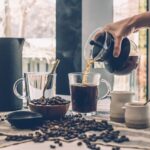 Freshly brewed aeropress coffee in a mug beside the plunger and brewing chamber on a kitchen counter