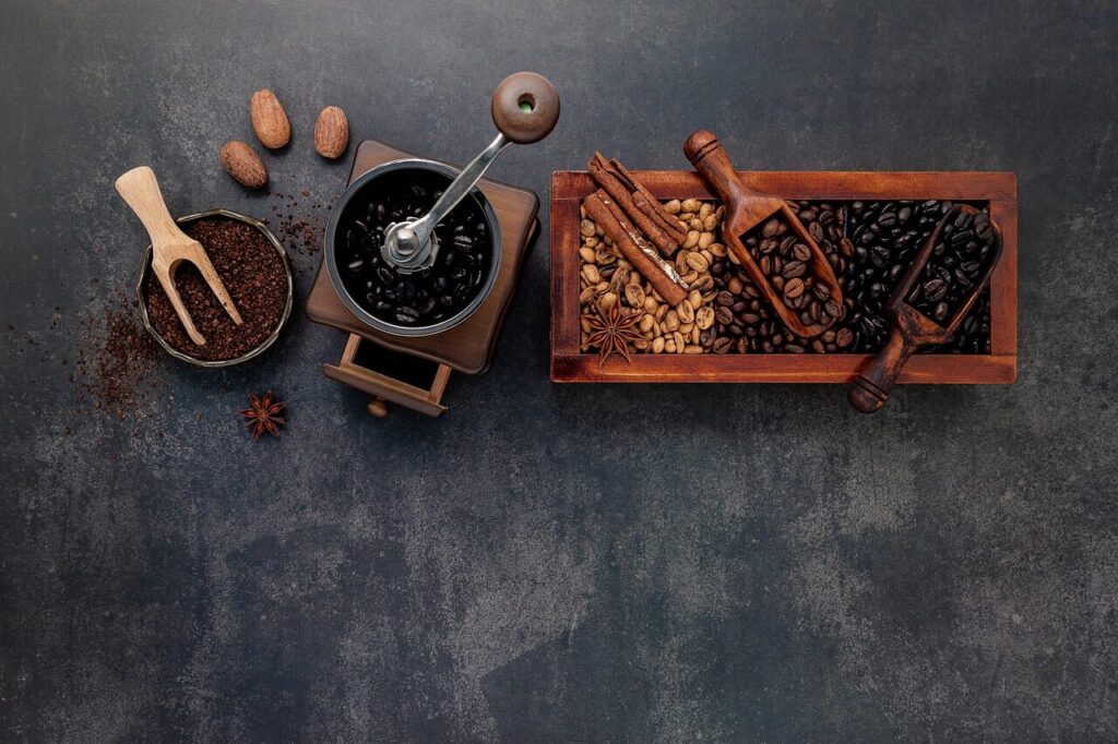 Hand grinder with whole roasted beans and freshly ground coffee on a counter