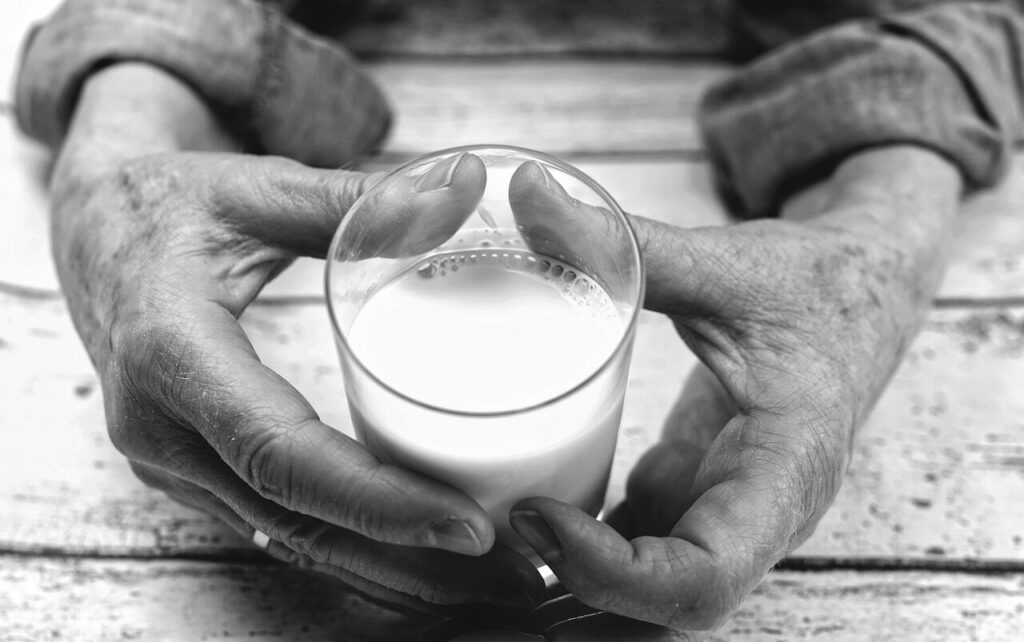 Hands holding a glass jar of milk with foam forming inside