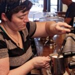 Hands holding a pitcher to steam milk for latte with an espresso machine wand