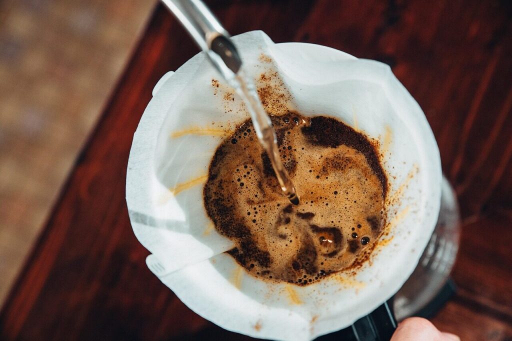 Hot water pouring from a gooseneck kettle over ground coffee in a paper filter