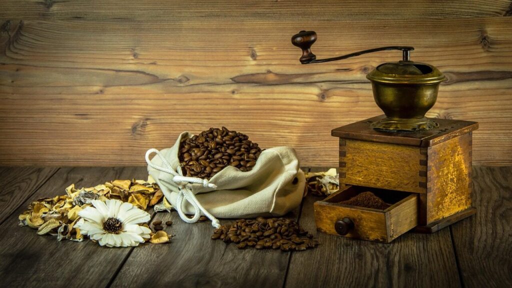 Whole roasted beans being scooped into a hand grinder before brewing