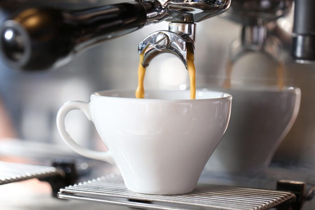 Barista holding a steam wand in a pitcher of milk beside an espresso machine